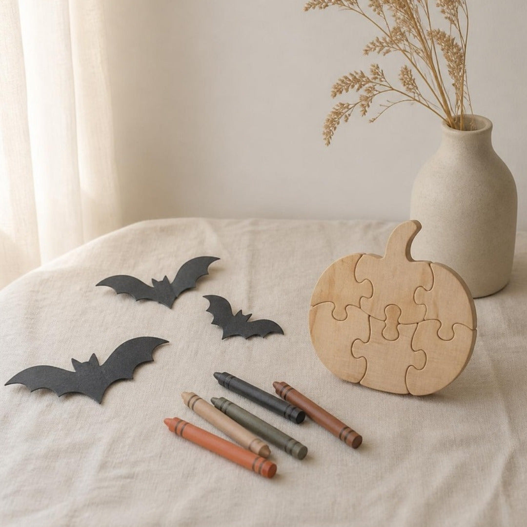 Paper bats, crayons and a wooden pumpkin-shaped puzzle on cream linen