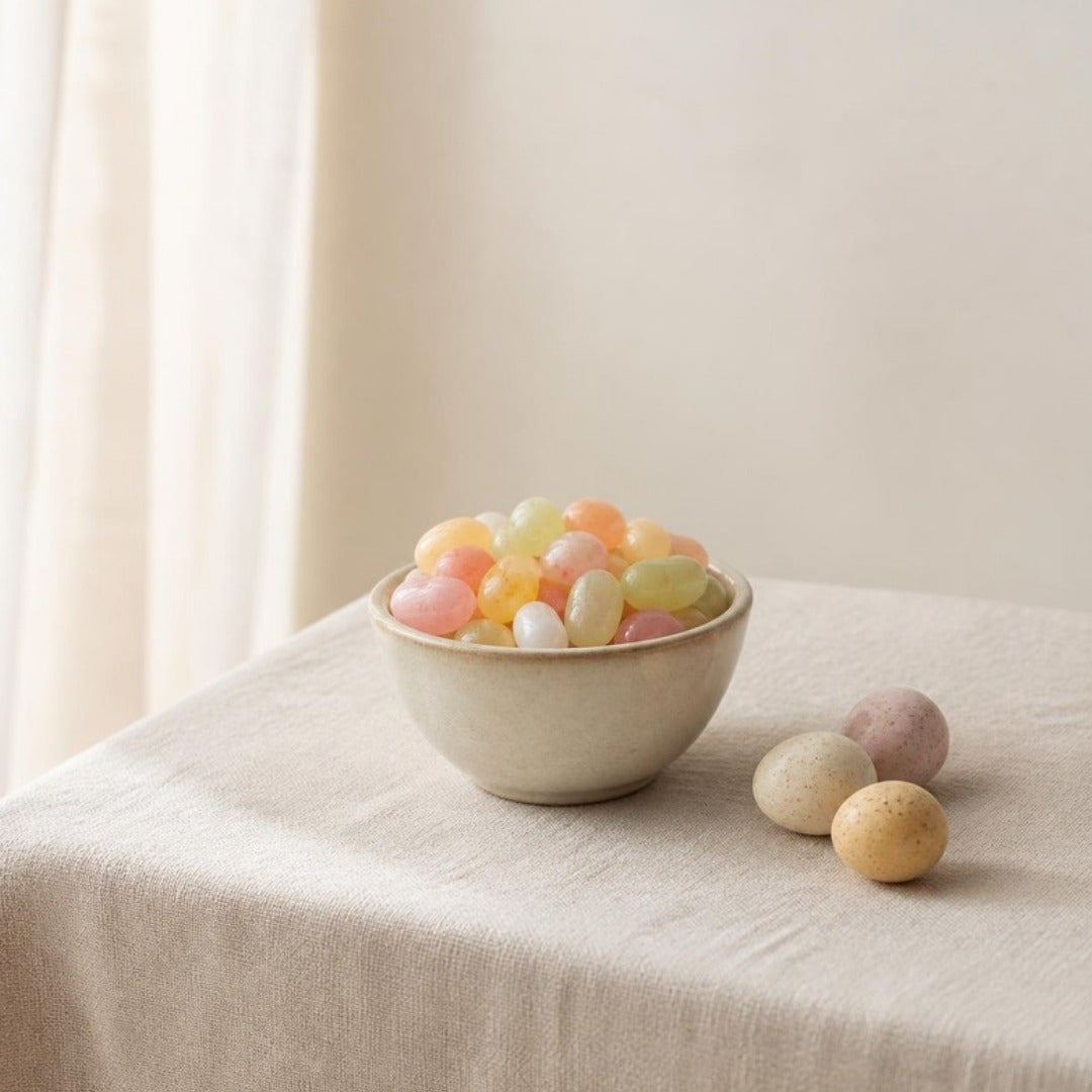 A bowl of pastel jelly beans and speckled candy eggs on cream linen