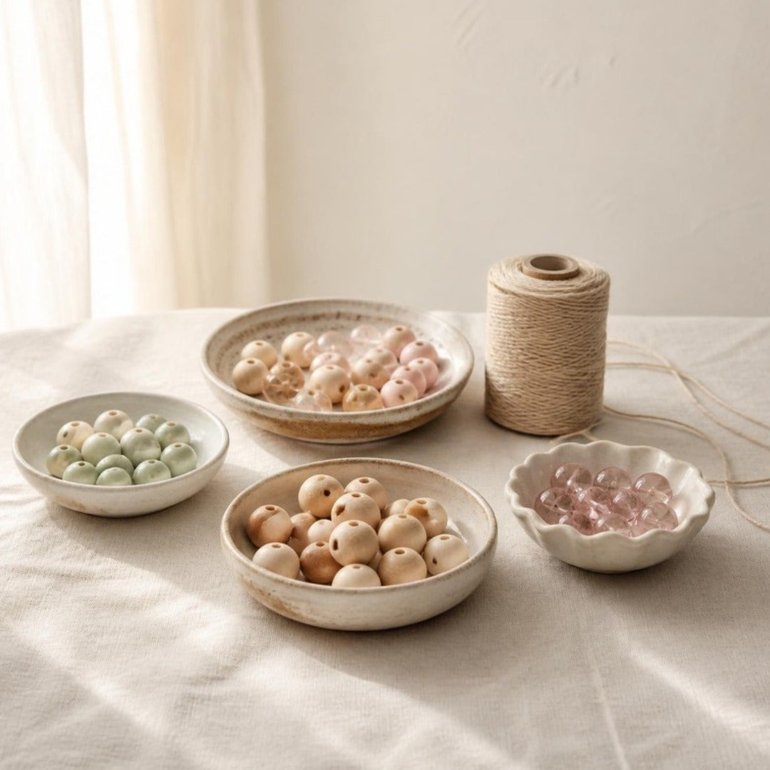 Ceramic dishes of wooden and glass beads in soft pastels with a spool of string on cream linen